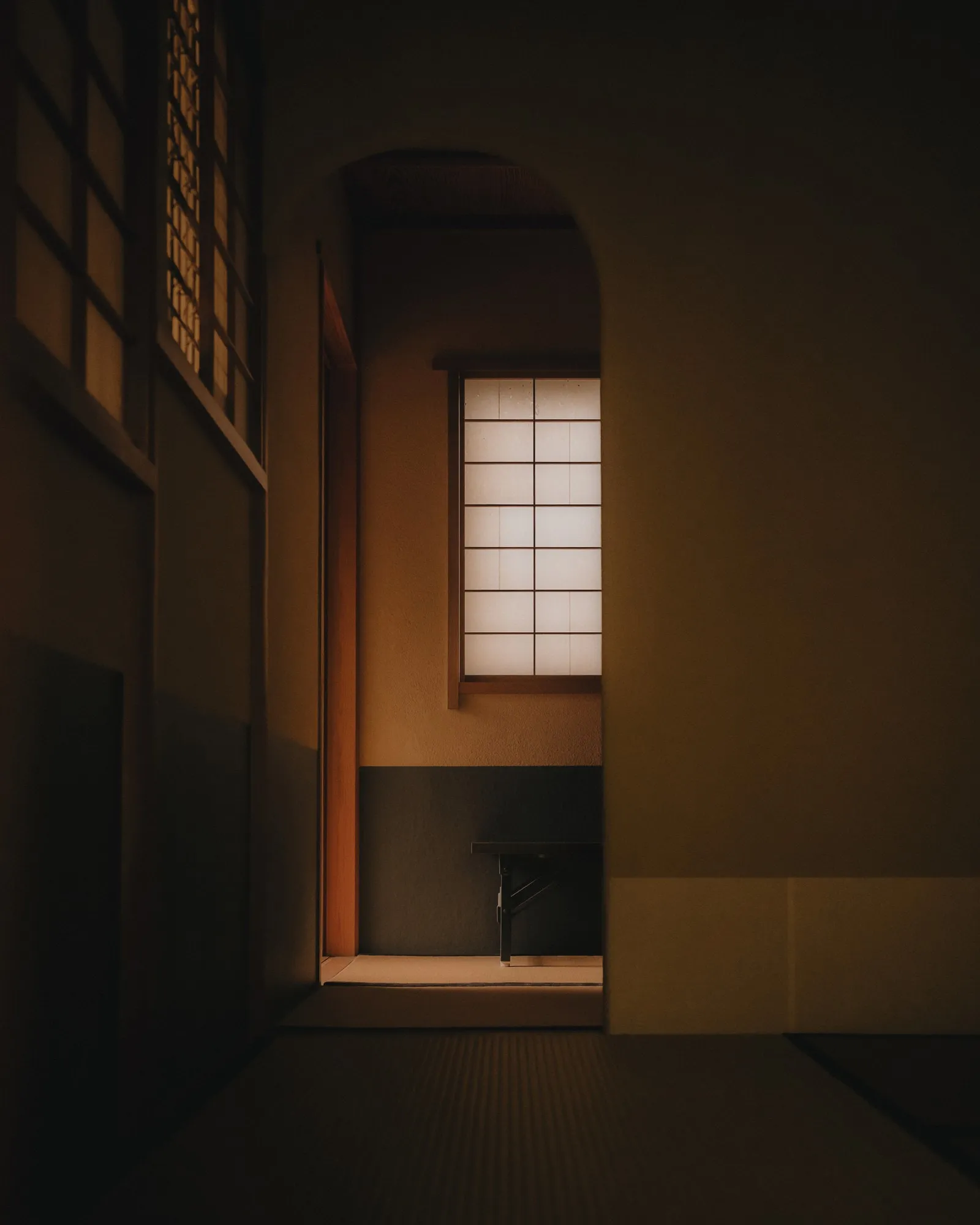 A Japanese tea room, a shoji window lit from outside beyond an arched doorway