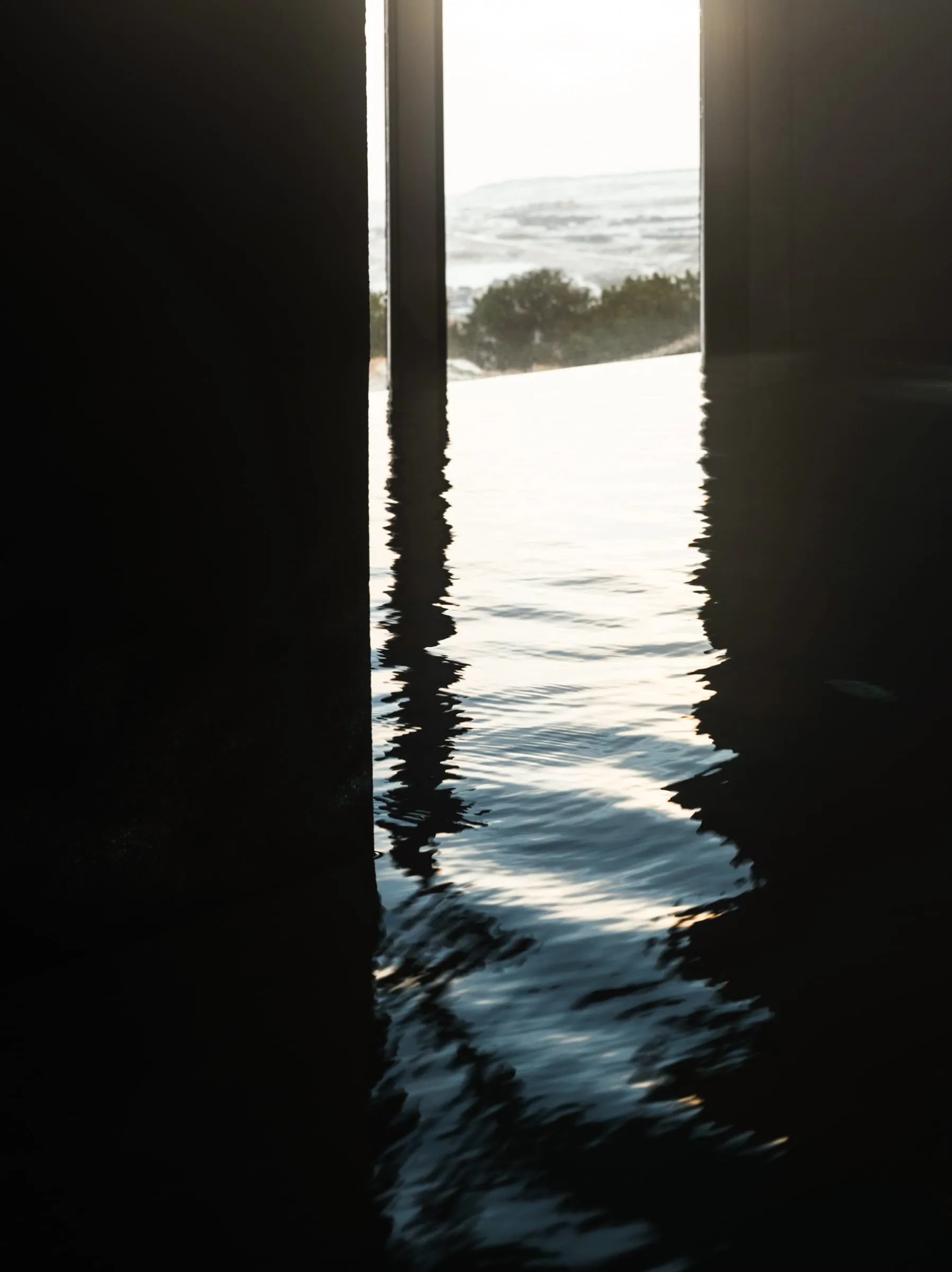 The pool meeting the glass wall with the town below, and the dark water of the indoor pool